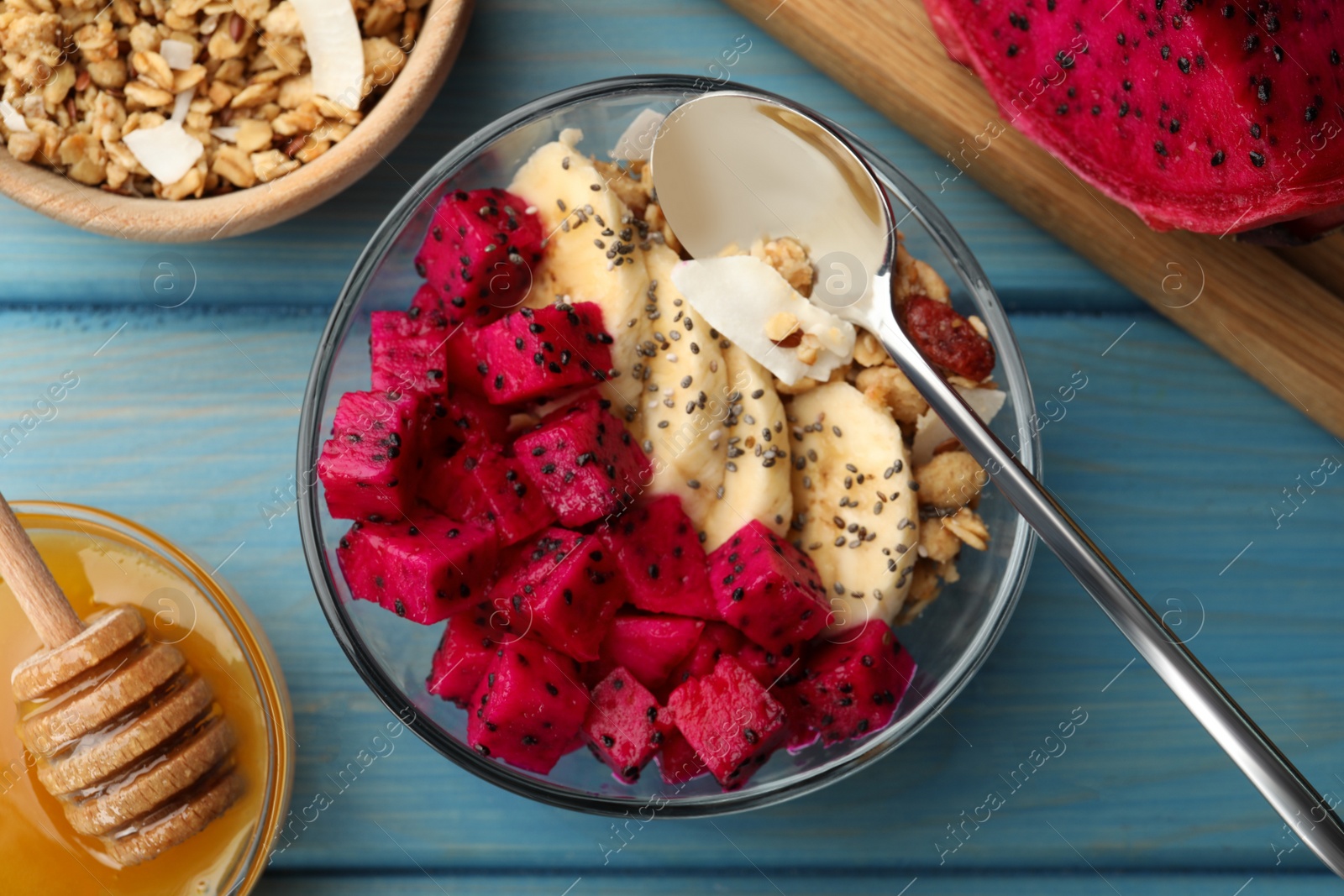 Photo of Bowl of granola with pitahaya and banana served on light blue wooden table, flat lay