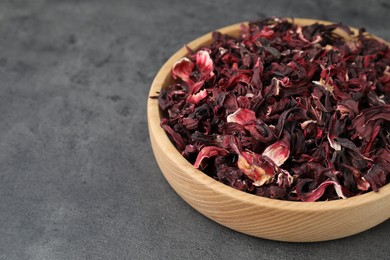 Photo of Hibiscus tea. Wooden bowl with dried roselle calyces on grey table, closeup. Space for text
