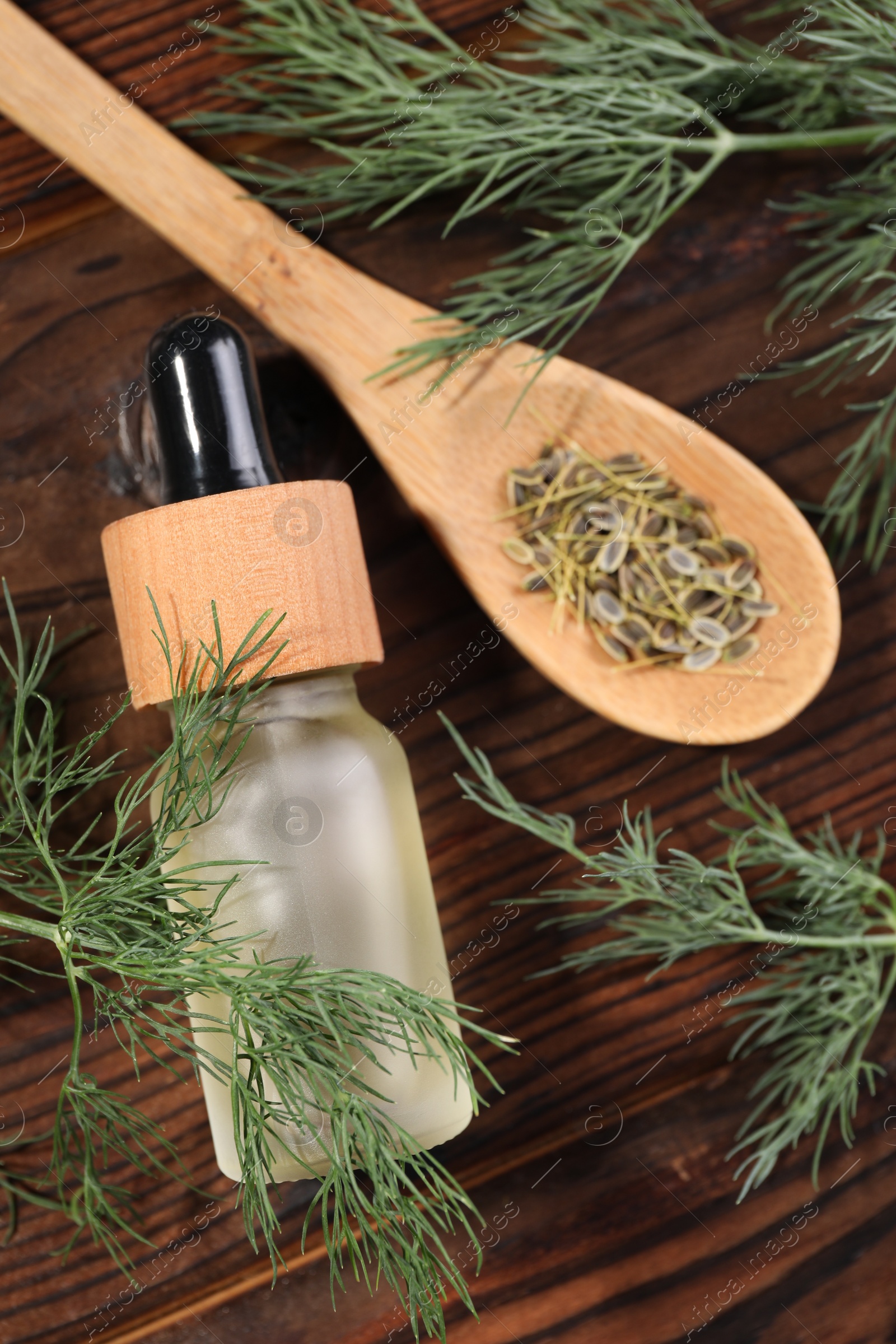 Photo of Bottle of essential oil and fresh dill on wooden table, flat lay