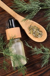 Bottle of essential oil and fresh dill on wooden table, flat lay