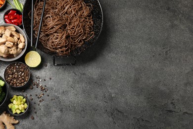 Wok with noodles, chicken and other products on grey table, flat lay. Space for text