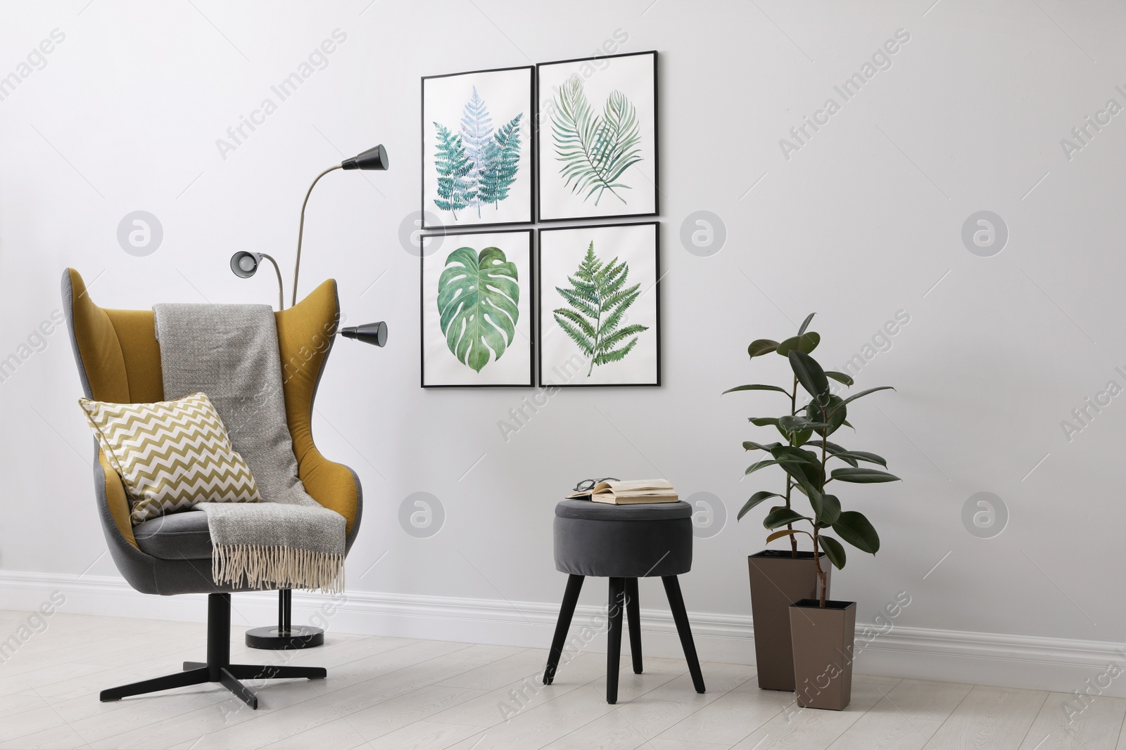 Photo of Stylish room interior with comfortable armchair and paintings of tropical leaves