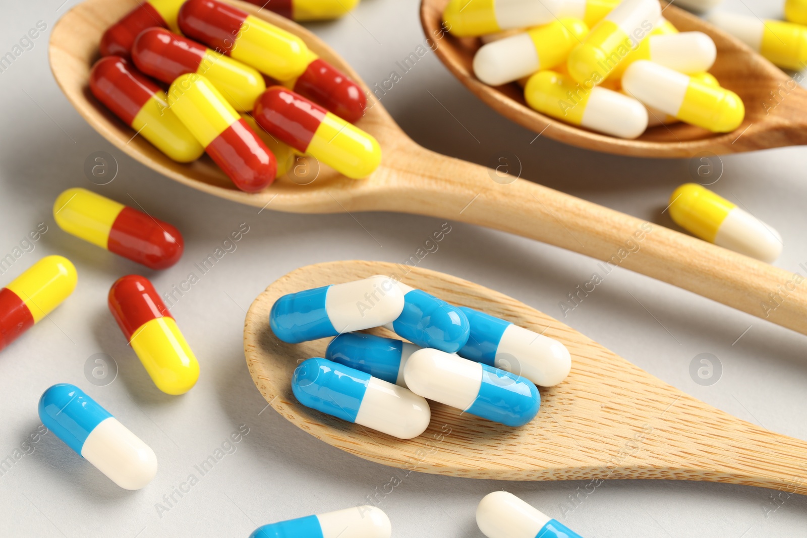 Photo of Many antibiotic pills with wooden spoons on grey background, closeup. Medicinal treatment