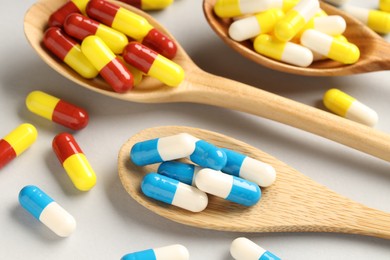 Photo of Many antibiotic pills with wooden spoons on grey background, closeup. Medicinal treatment