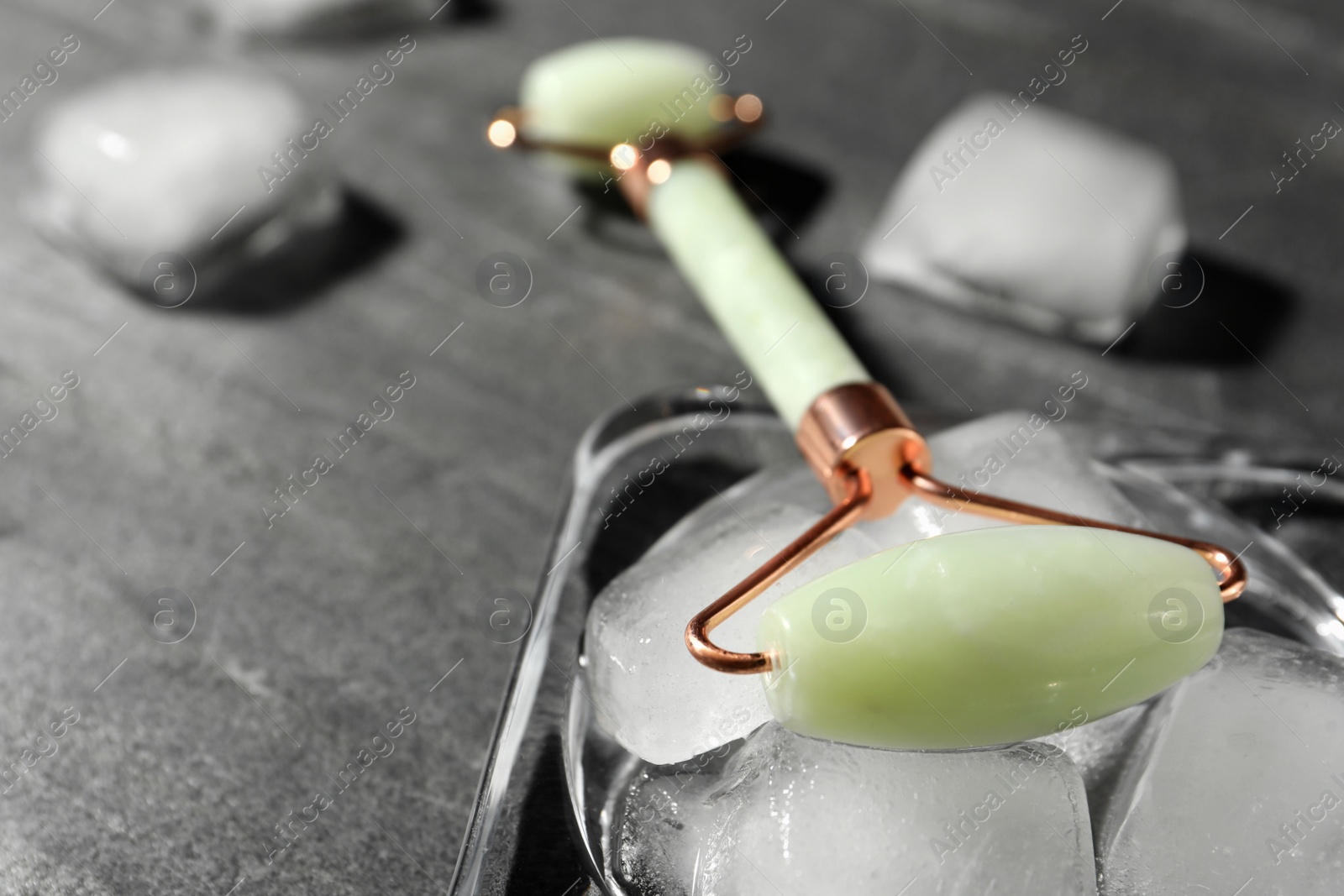 Photo of Natural jade face roller and ice cubes on grey background, closeup