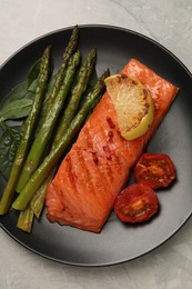 Photo of Tasty grilled salmon with tomatoes, lemon and asparagus on grey table, top view