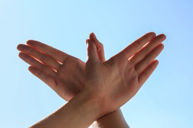 Woman making hand gesture like bird on light blue background, closeup