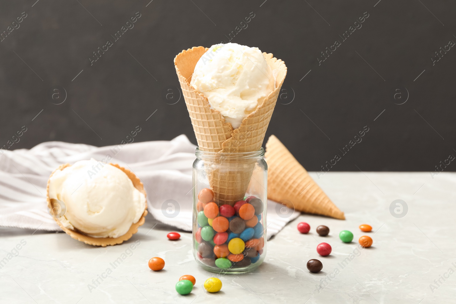 Photo of Delicious vanilla ice cream in wafer cone with candies on light grey table