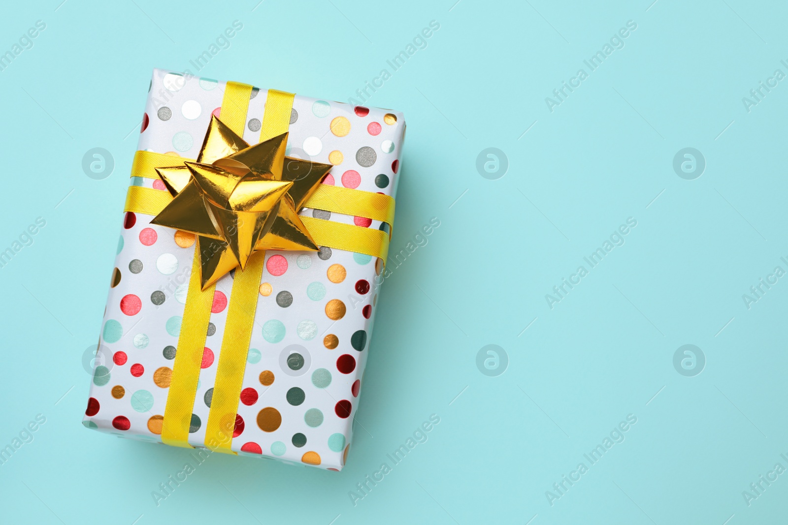 Photo of Beautifully wrapped gift box on turquoise background, top view. Space for text