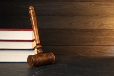 Photo of Wooden gavel and stack of books on dark textured table. Space for text