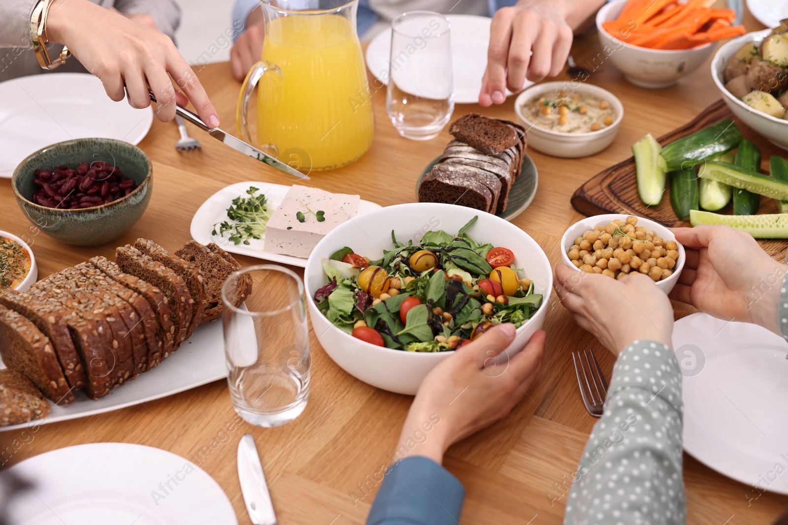 Photo of Friends eating vegetarian food at wooden table indoors, closeup