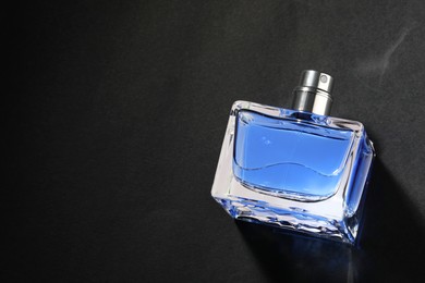 Photo of Blue men's perfume in bottle on black background, top view. Space for text