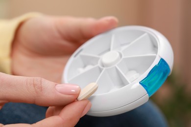 Photo of Woman taking pill from plastic box indoors, closeup