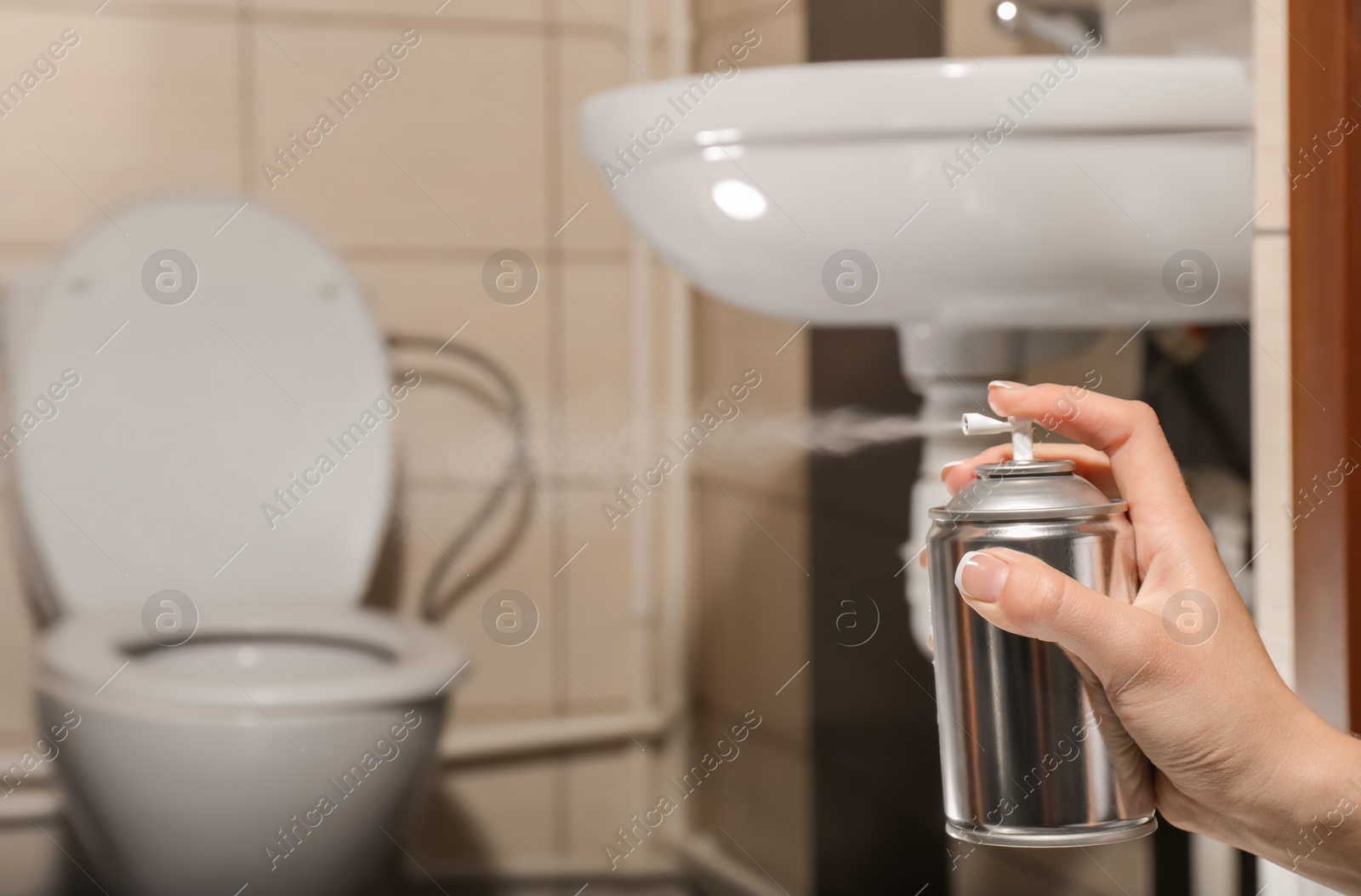 Photo of Woman spraying air freshener in bathroom