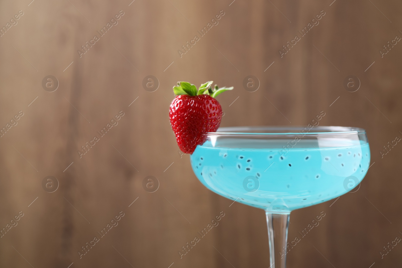 Photo of Refreshing light blue cocktail with strawberry on blurred background, space for text