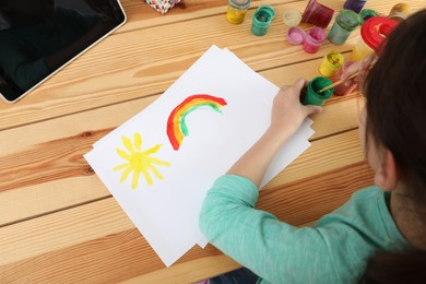 Photo of Little girl drawing on paper with paints at online lesson indoors, above view. Distance learning