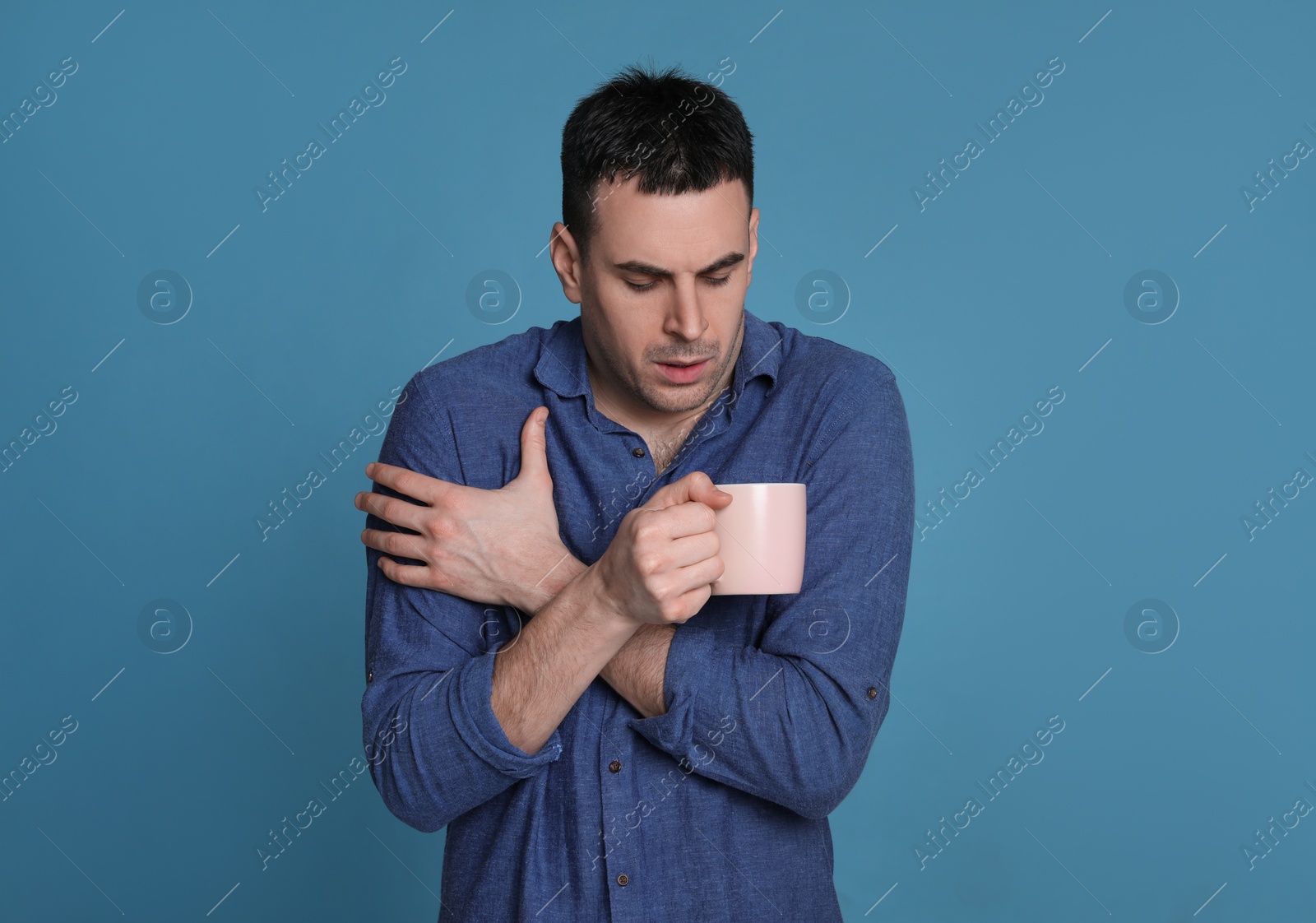 Photo of Young man with cup of hot drink suffering from fever on blue background. Cold symptoms
