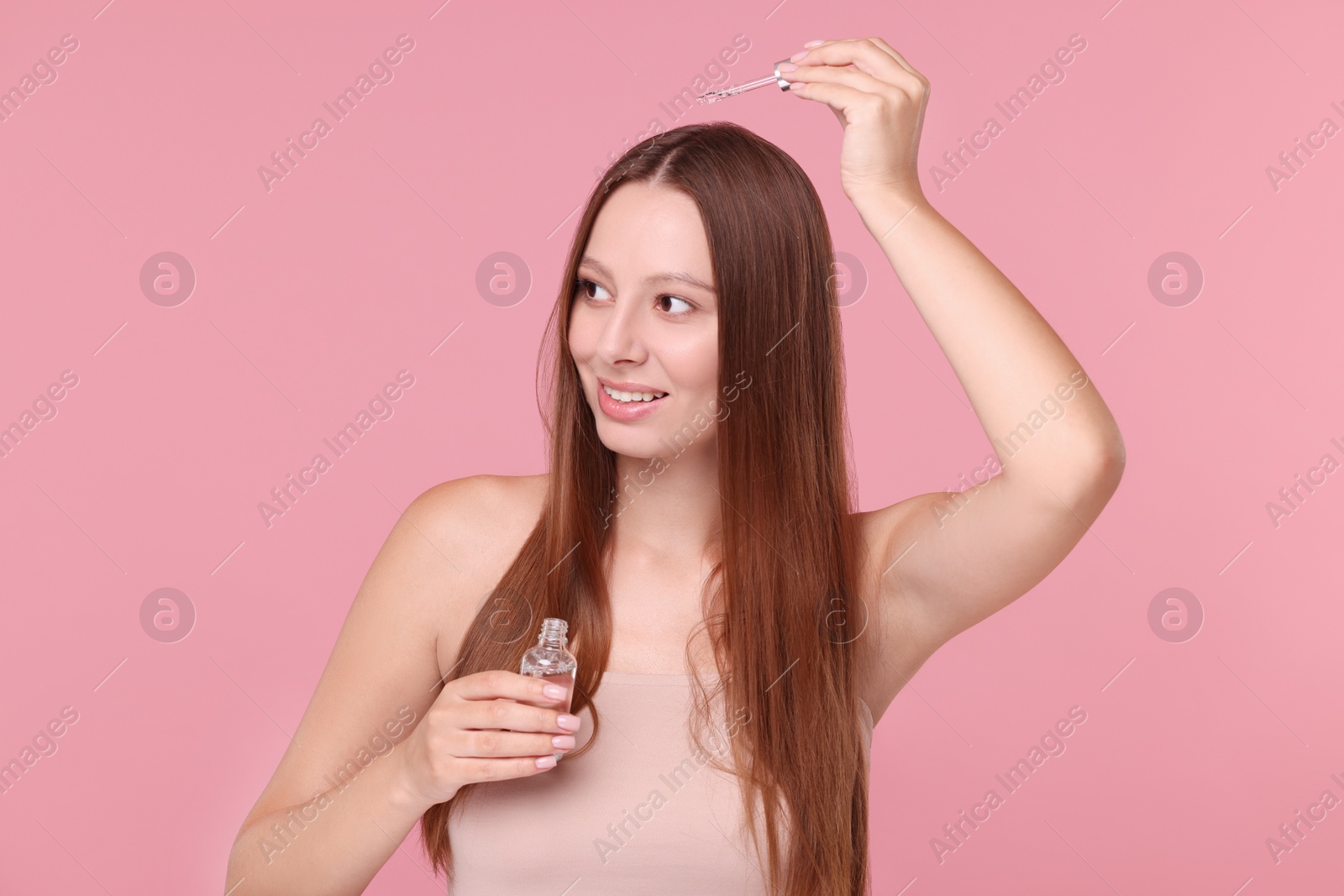 Photo of Beautiful woman applying serum onto hair on pink background