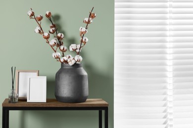 Branches with white fluffy cotton flowers on console table in cozy room. Interior design