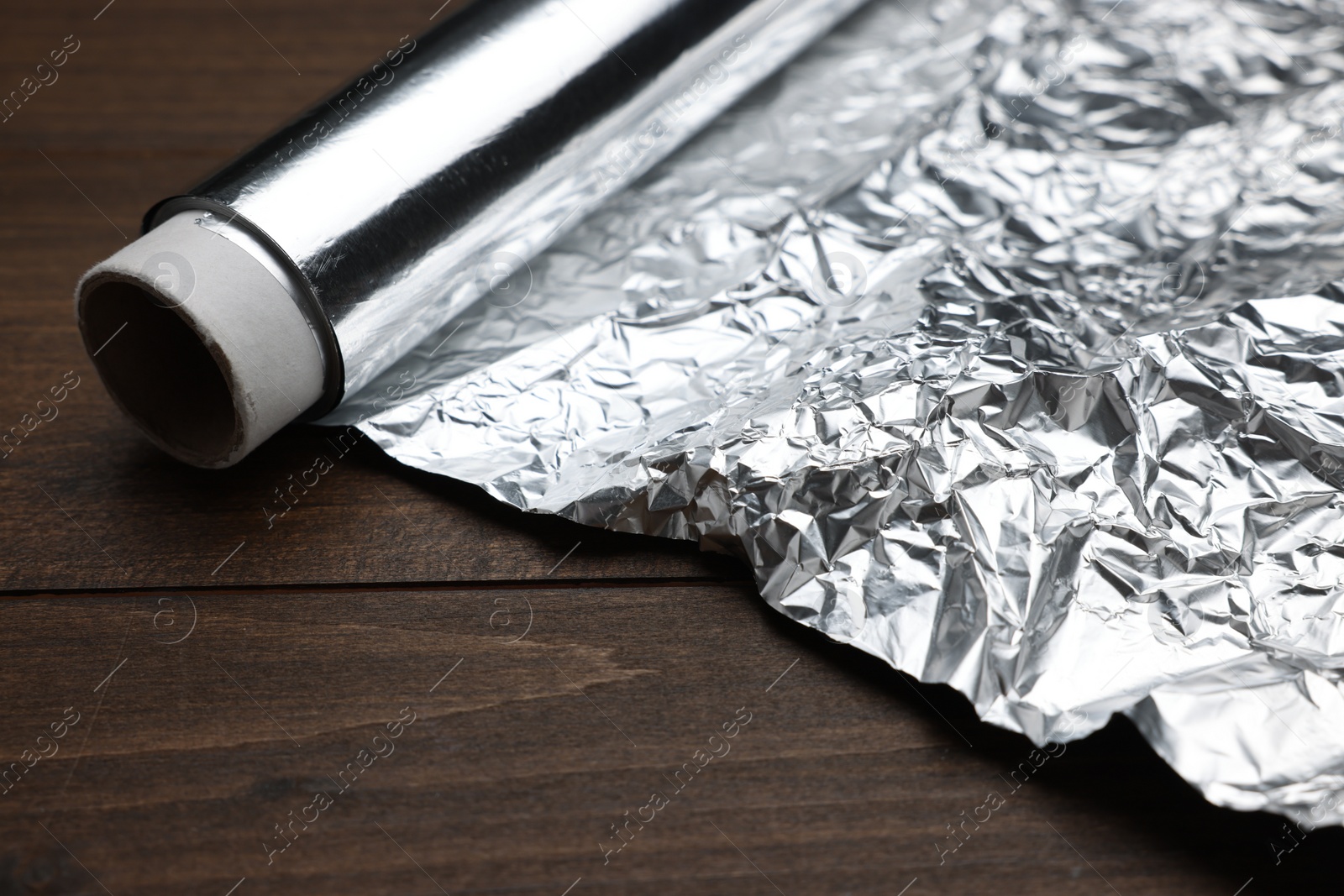 Photo of Roll of foil paper on wooden table, closeup