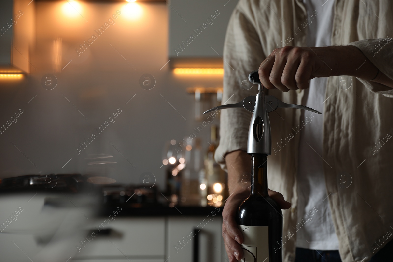 Photo of Man opening wine bottle with corkscrew in kitchen, closeup. Space for text