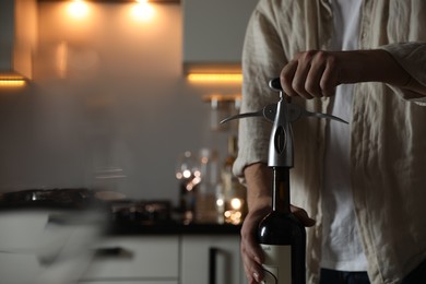 Photo of Man opening wine bottle with corkscrew in kitchen, closeup. Space for text