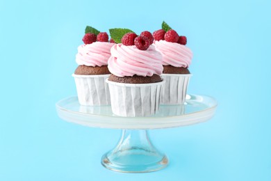 Photo of Delicious cupcakes with cream and raspberries on light blue background