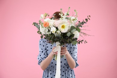 Photo of Woman covering her face with bouquet of beautiful flowers on pink background
