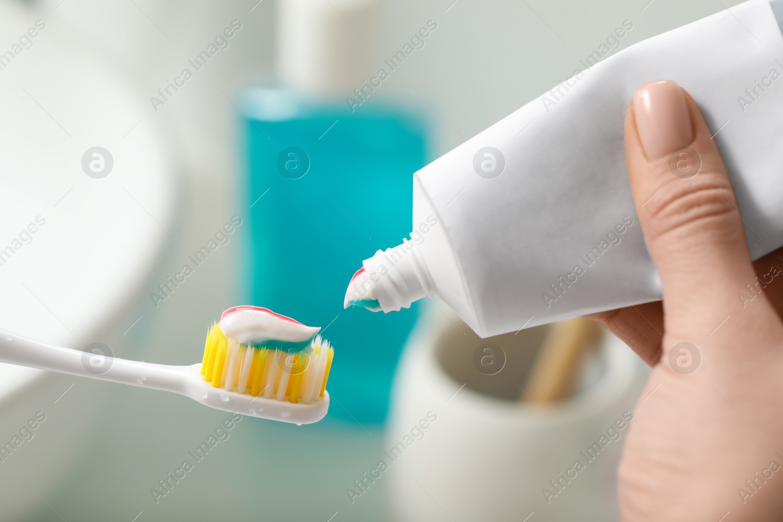 Photo of Woman applying toothpaste on brush against blurred background, closeup