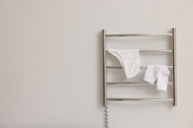 Photo of Heated towel rail with underwear and socks on white wall in bathroom, space for text