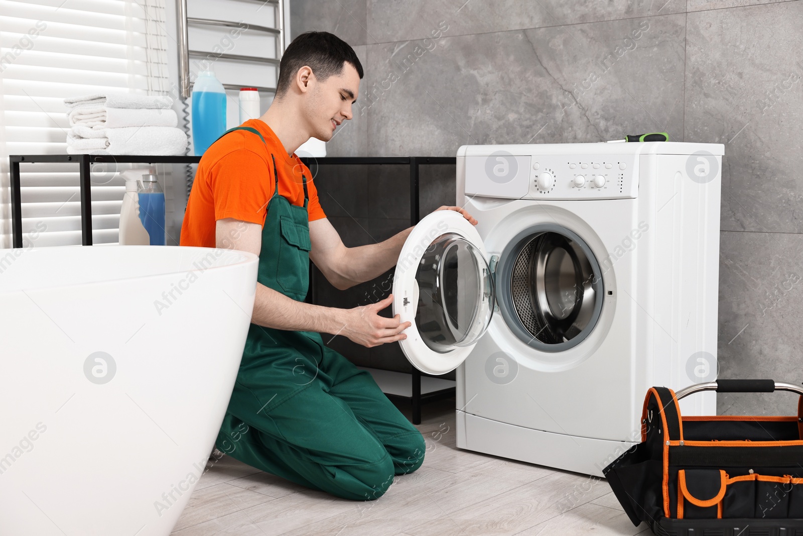 Photo of Young plumber repairing washing machine in bathroom