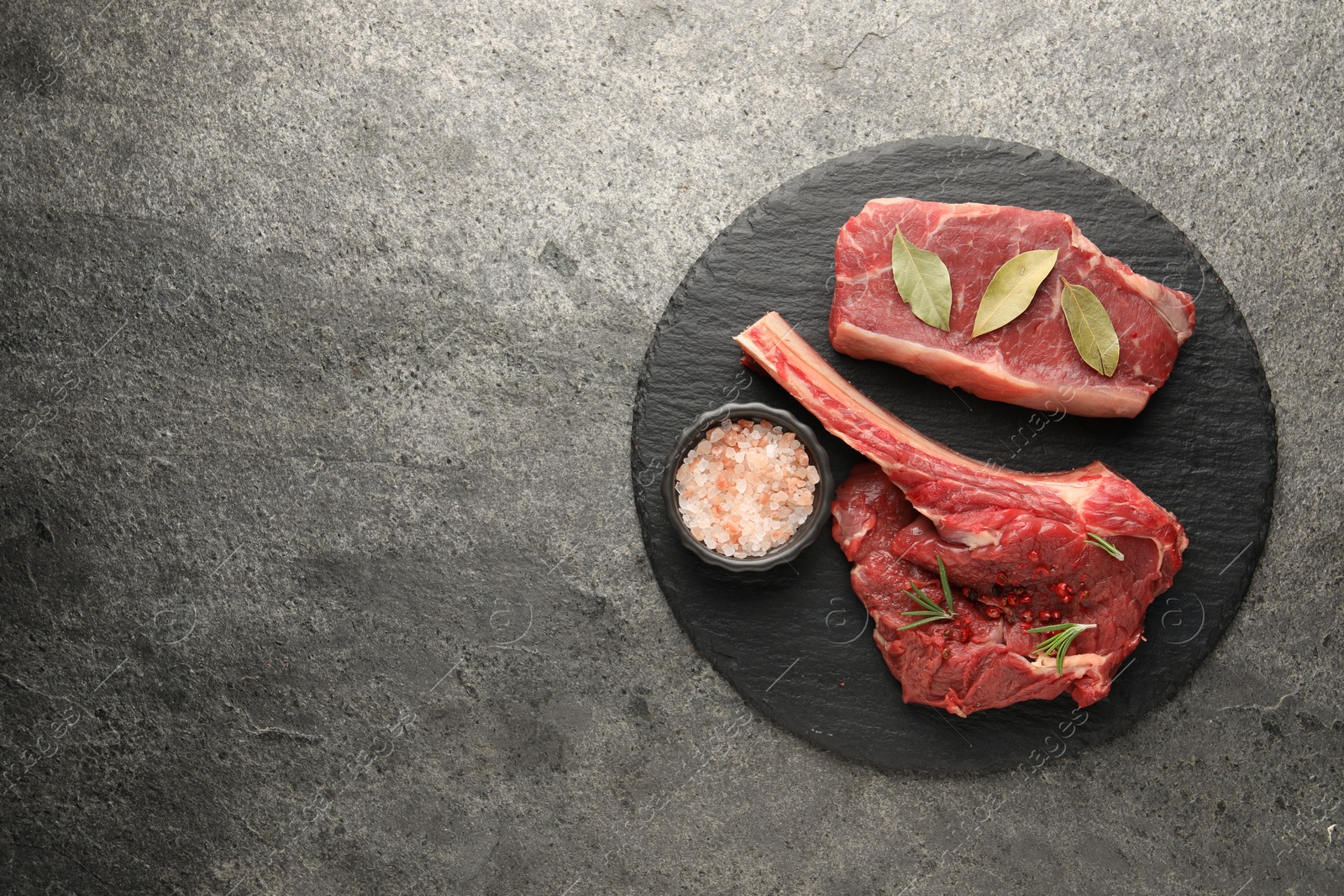 Photo of Pieces of raw beef meat and spices on grey textured table, top view. Space for text