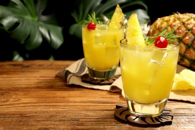 Photo of Glasses of tasty pineapple cocktail with rosemary and cherry on wooden table. Space for text