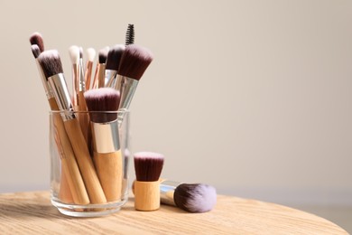 Set of professional makeup brushes on wooden table against beige background, space for text