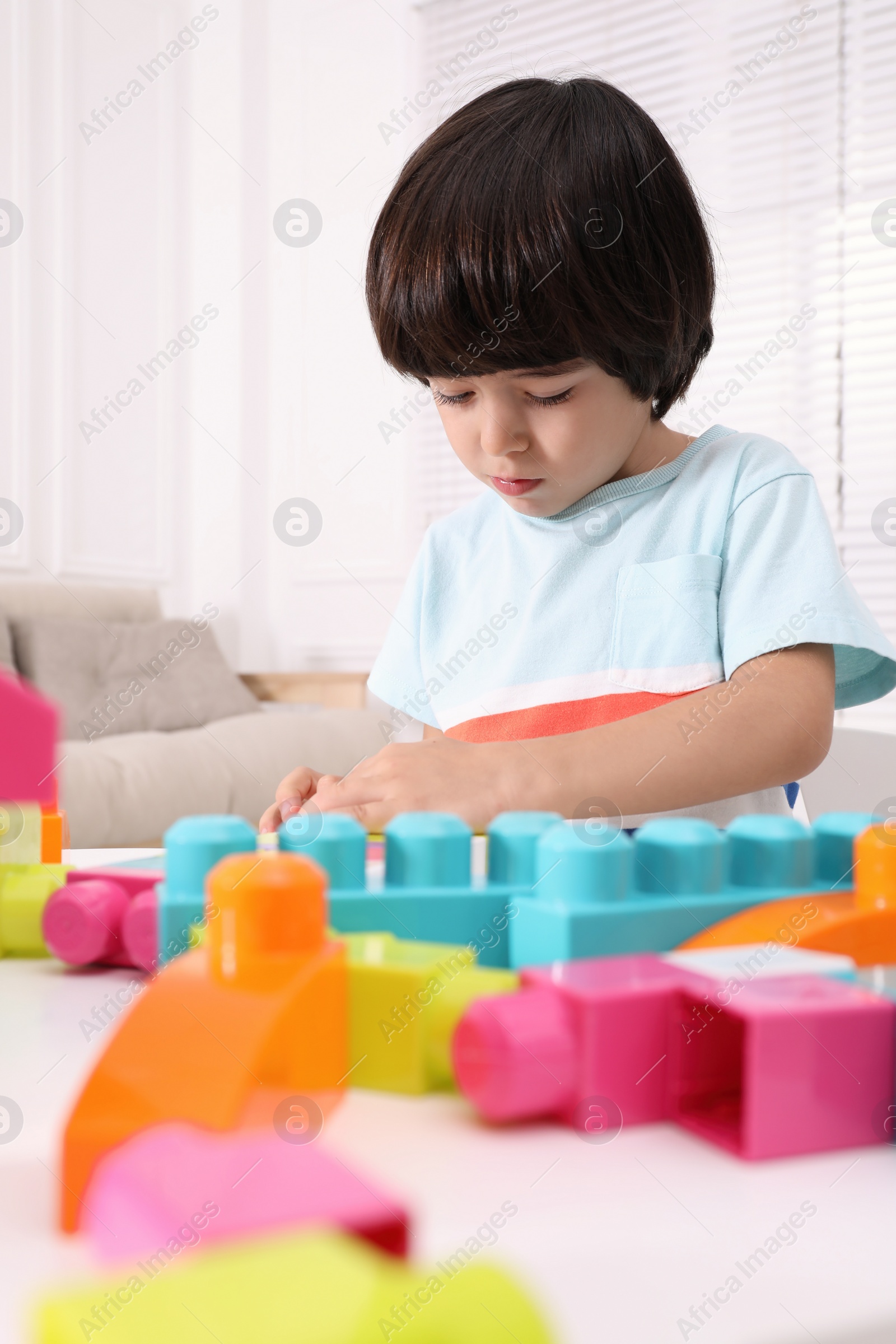 Photo of Cute little boy playing with colorful building blocks at table in living room