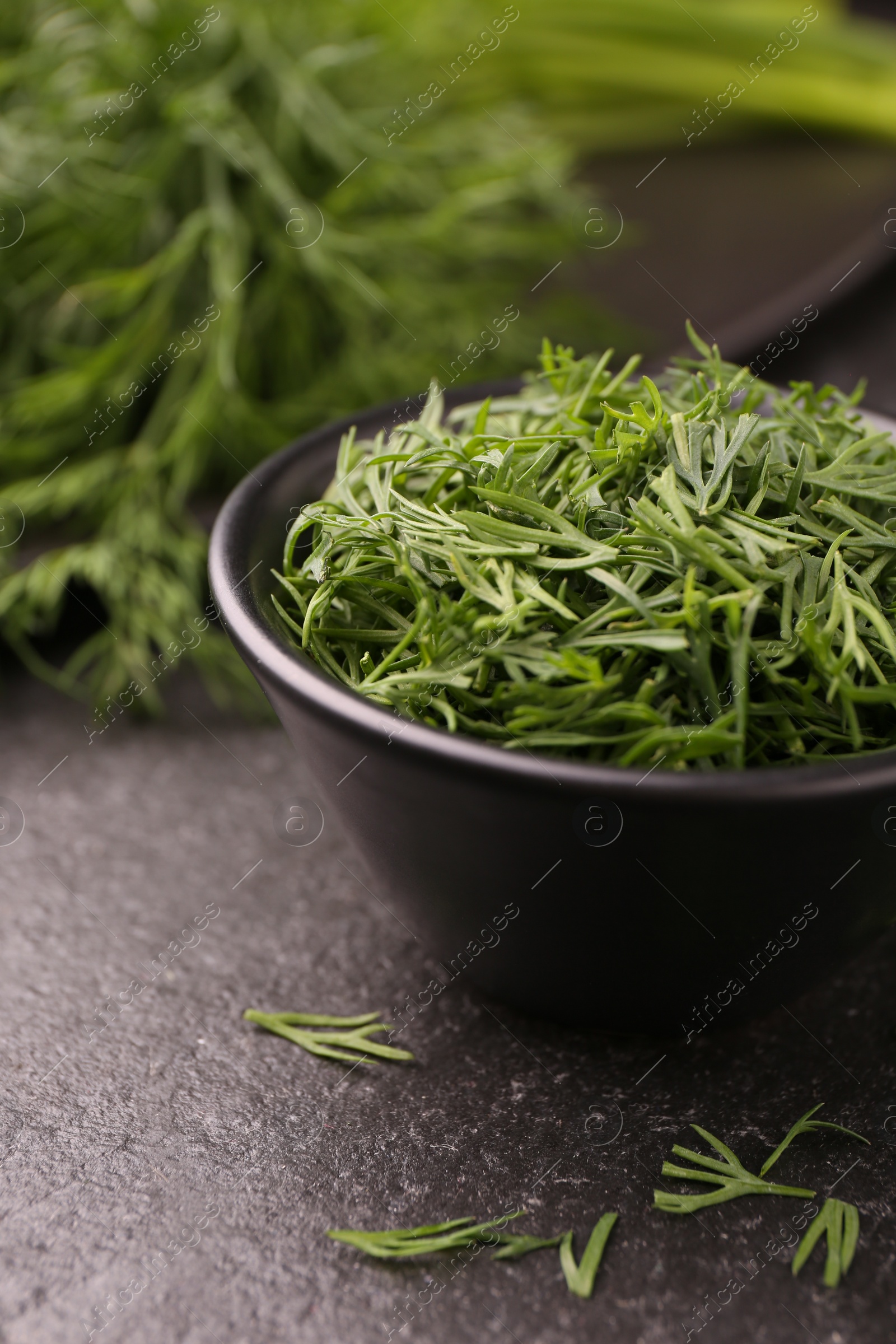 Photo of Fresh cut dill in bowl on dark textured table, closeup