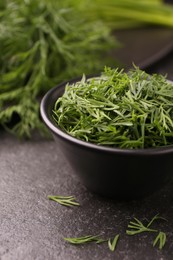 Photo of Fresh cut dill in bowl on dark textured table, closeup