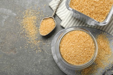 Photo of Brown sugar and spoon on grey textured table, flat lay. Space for text