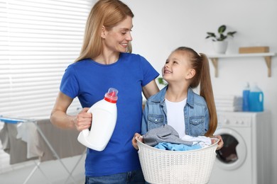 Mother and daughter holding basket with dirty clothes and fabric softener in bathroom