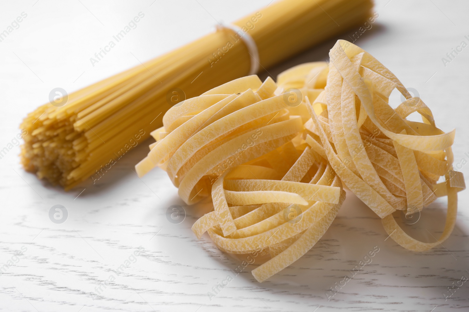 Photo of Tagliatelle pasta and spaghetti on white wooden table, closeup