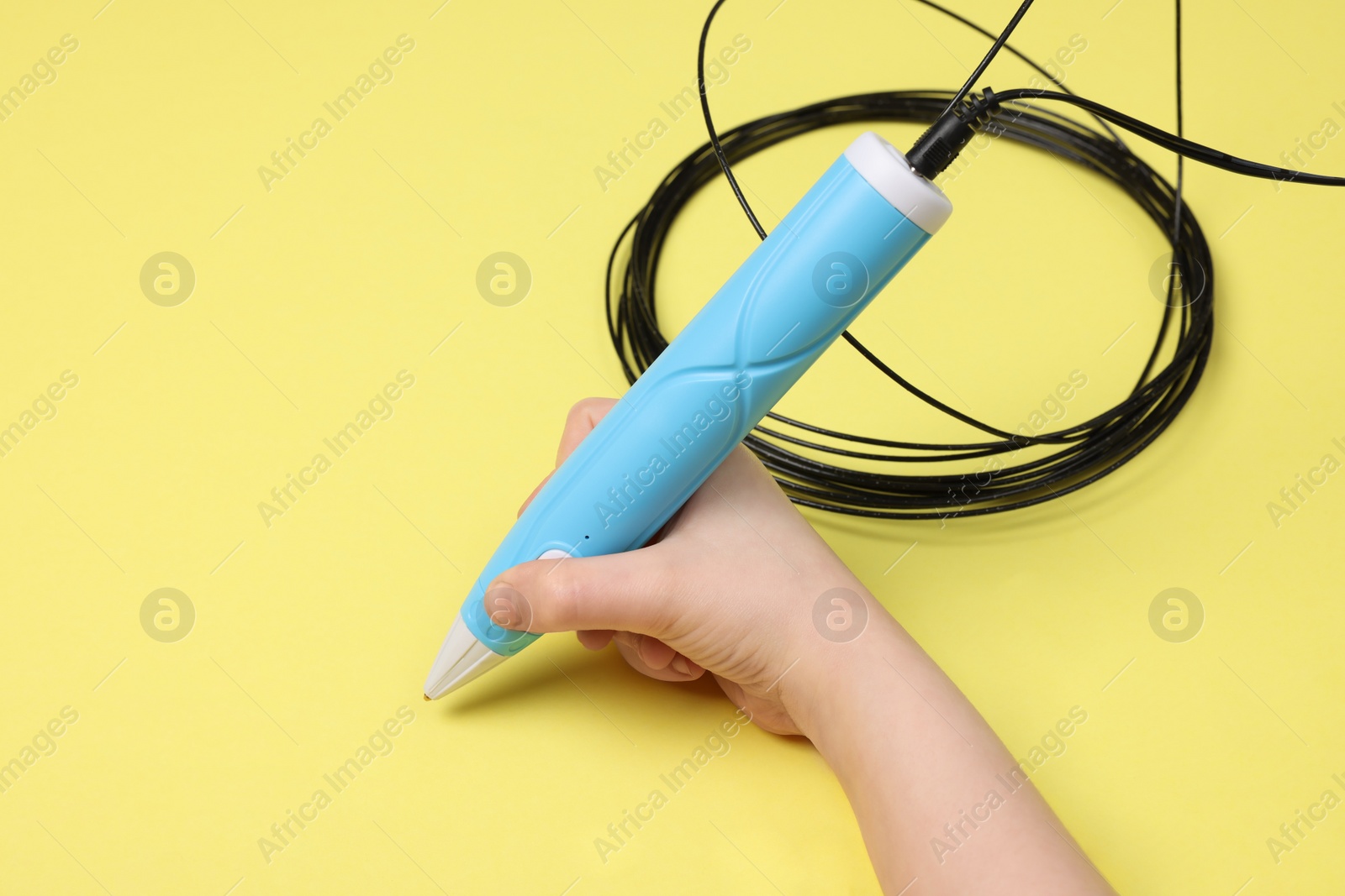 Photo of Boy drawing with stylish 3D pen on yellow background, closeup