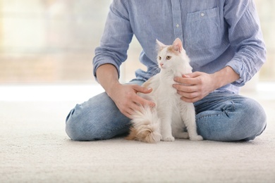 Photo of Young man with cute cat sitting on floor at home