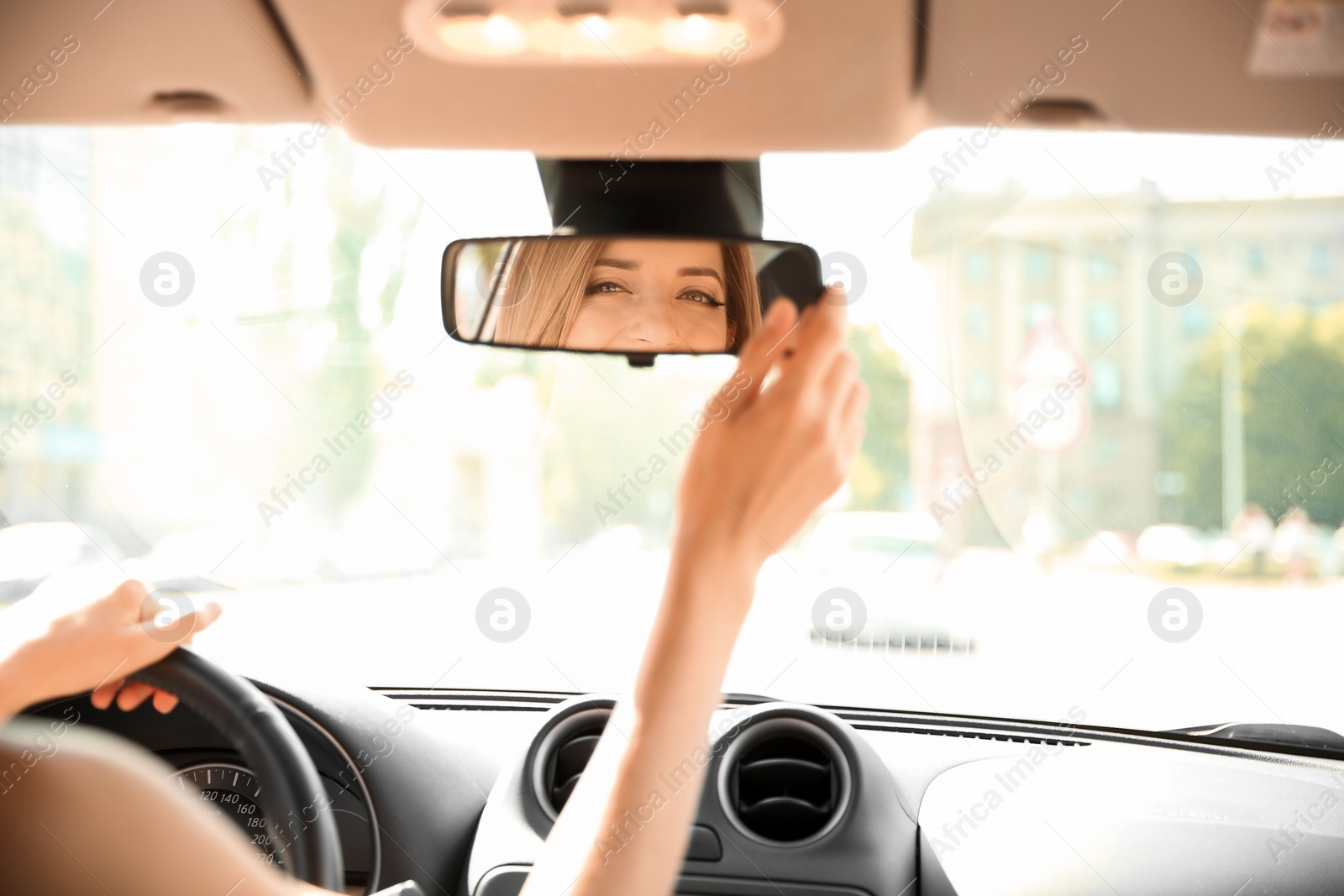 Photo of Young woman adjusting rearview mirror in car