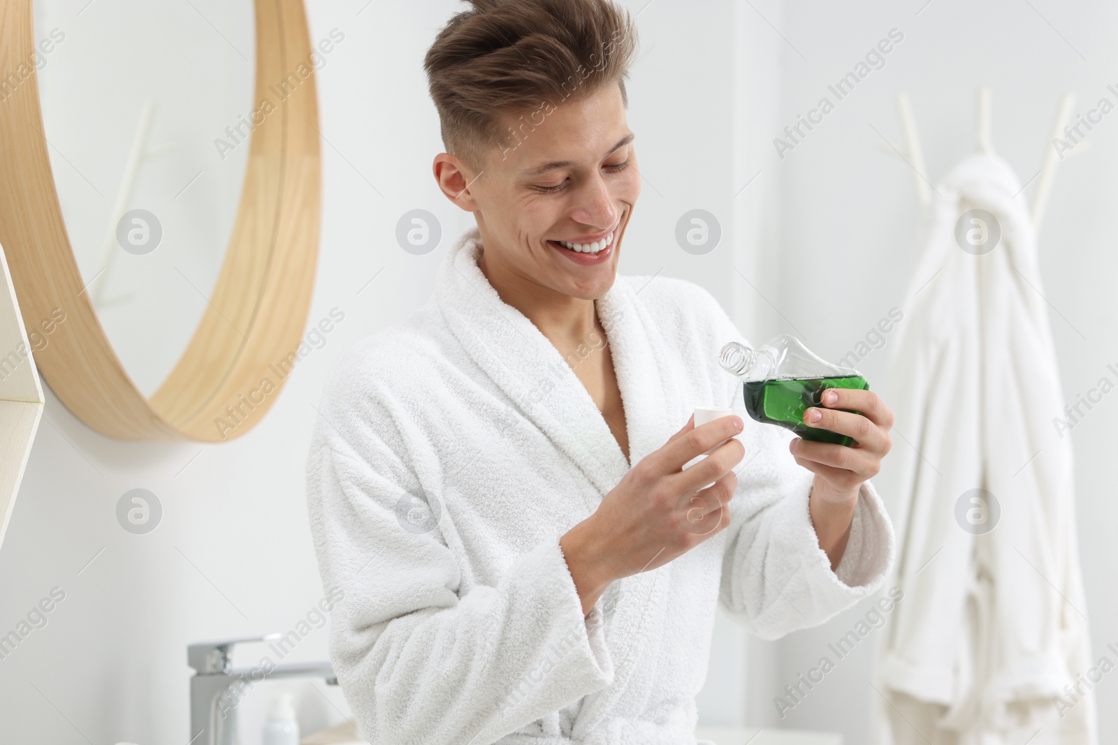 Photo of Young man using mouthwash in bathroom. Oral hygiene