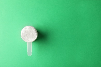 Scoop of protein powder on green background, top view with space for text