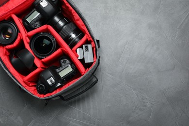 Photo of Professional photography equipment in backpack on grey stone table, top view. Space for text