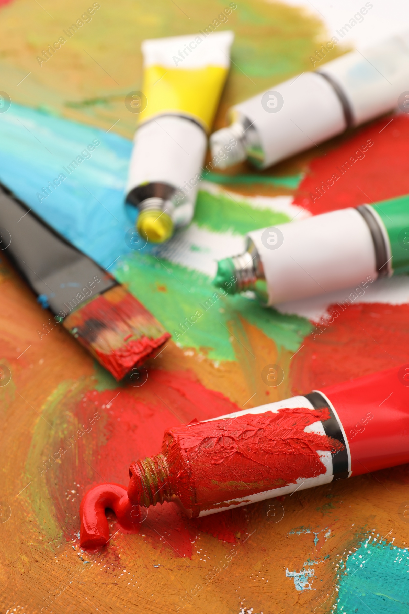 Photo of Tubes of colorful oil paints, brush on canvas with abstract painting, closeup