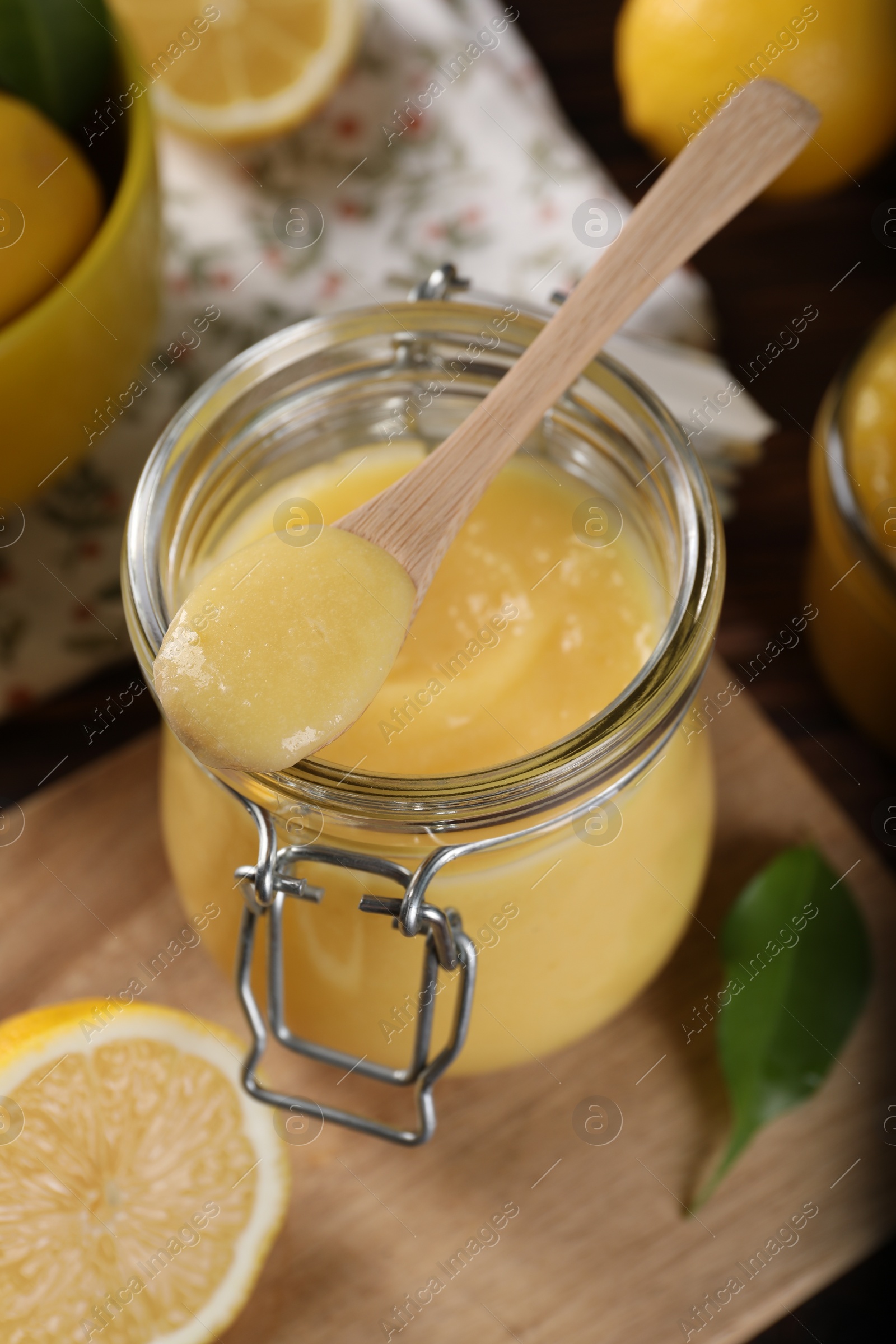 Photo of Delicious lemon curd in glass jar, spoon and fresh citrus fruits on table