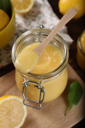 Delicious lemon curd in glass jar, spoon and fresh citrus fruits on table