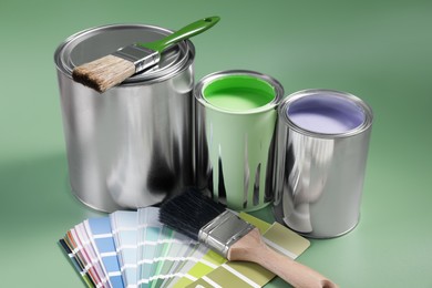 Photo of Cans of paints, palette and brushes on light green background